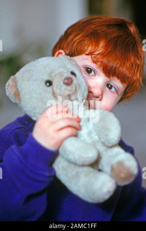 Timido ragazzino di capelli rossi che tiene un orsacchiotto Foto Stock