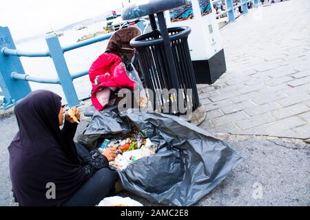 Donna siriana che indossa burqa nero alla ricerca di cibo da immondizia con i suoi bambini. Sono sfuggiti alla guerra in Siria. Foto Stock