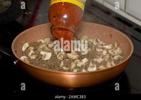 Aggiungere la salsa bolognese alla mince macinata di manzo e ai funghi cucinando in padella Foto Stock