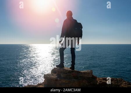backpacker in piedi sulla cima di una roccia vicino al mare, lente flare. Foto Stock