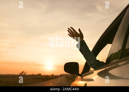 Sentire il vento mentre si guida attraverso la campagna, donna raggiungendo fuori mano dal finestrino in autunno il tramonto, il fuoco selettivo Foto Stock
