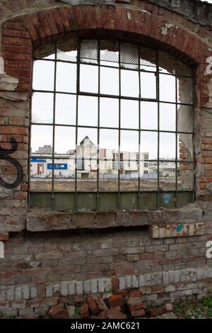 Una vista da una finestra di un edificio demolito, vecchia fabbrica. Parete resistente agli agenti atmosferici. Finestra rotta. Foto Stock