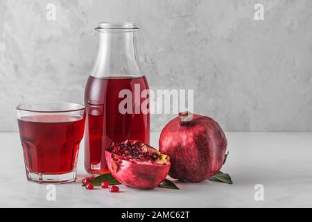 Succo di melograno in una bottiglia con bicchiere di succo e frutta fresca di melograno su un tavolo di marmo. Concetto di bevanda sana Foto Stock