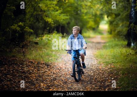 Ragazzo teen guida una bicicletta lungo un percorso nella foresta. Il ciclista scorre velocemente attraverso le molleggiate Foto Stock