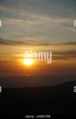 Tramonto mozzafiato sul mare con luce riflessa con una catena montuosa di fronte, nuvole scure nel cielo. Immagine verticale. Foto Stock