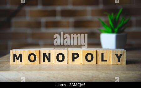 Monopolio scritto su un cubo di legno su sfondo di mattoni. Foto Stock