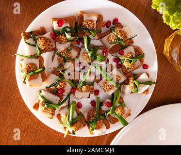Panini con pancetta grassa, legati con frecce con cipolle verdi e grani di senape e melograno rosso. Appetitose tapas con lardo e spezie, Medite Foto Stock