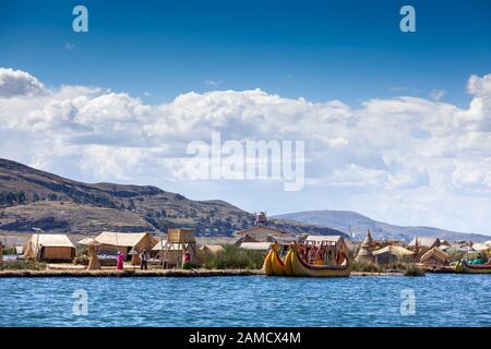 Isole galleggianti di Uros sul lago Titicaca in Perù, Sud America - 2019-12-01. Sull'isola ci sono un uomo locale e due donne, accanto ad una barca turistica Foto Stock