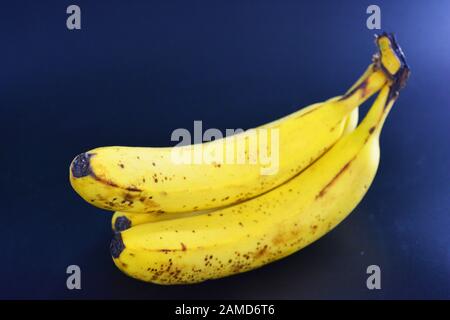 Le banane gialle mature dolci, un mazzo di tre banane con macchie nere di pegmet si trovano su uno sfondo di plastica nera. Nutrizione adeguata, sana saporita Foto Stock