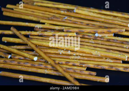 Cannucce saporite e salate con sale fatto di farina, sneking sparse su uno sfondo di plastica nera. Foto Stock