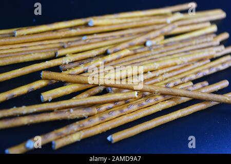 Cannucce saporite e salate con sale fatto di farina, sneking sparse su uno sfondo di plastica nera. Foto Stock