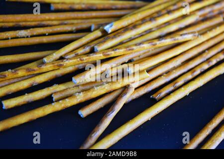 Cannucce saporite e salate con sale fatto di farina, sneking sparse su uno sfondo di plastica nera. Foto Stock