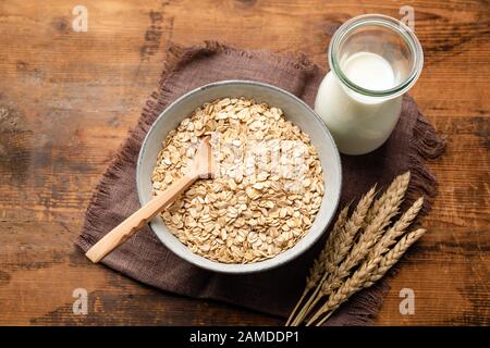 Fiocchi di avena secchi, farinata d'avena, avena arrotolata e bottiglia di latte di avena su uno sfondo di legno. Sano vegano, cibo vegetariano. Mangiare pulito, stare, perdita di peso Foto Stock