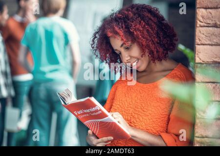 Curly red-haired studente sensazione coinvolto nella lettura libro Chinse Foto Stock