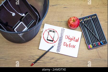 Messaggio detox digitale sul blocco note sulla scrivania accanto a dispositivi, tablet e smartphone, nel cestino rifiuti sulla scrivania, vista dall'alto. Foto Stock