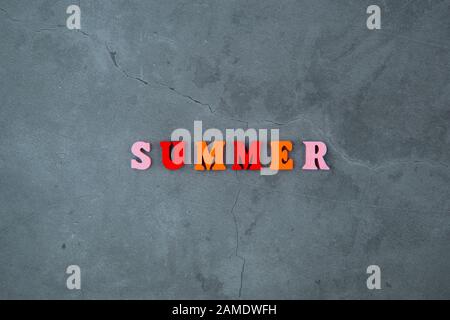 Il variopinto estate parola è fatta di lettere in legno su un grigio muro intonacato sfondo Foto Stock