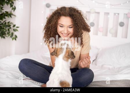 Ragazza sorridente teenage che gioca con il suo cane in camera da letto Foto Stock