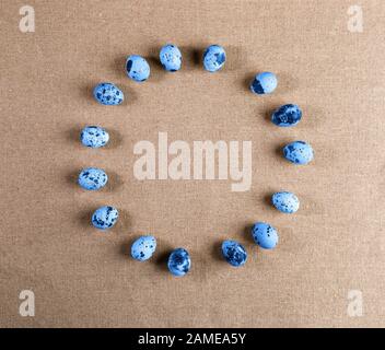 Set di uova di quaglia macchiate, colorate in colori alla moda del 2020 Classic Blue, adagiate in cerchio su tela rustica ruvida. Vista dall'alto, disposizione piatta, spazio di copia. Tendenza Foto Stock