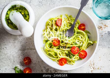 Zucchine con pesto, avocado e pomodori in un piatto bianco. Concetto di cibo vegano crudo. Foto Stock