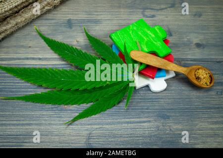 Tipi concettuali di prodotti di cannabis immagine concettuale con una foglia di cannabis, verde, rosso, blu e bianco puzzle in legno e piccolo cucchiaio di legno Foto Stock