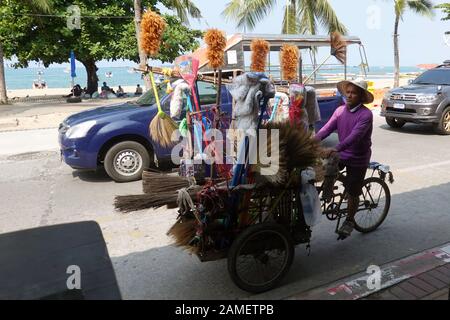 Pattaya, Tailandia - 24 Dicembre 2019: Venditore di attrezzature per la pulizia. Uomo bicicletta a cavallo con tutti i tipi di spazzole su Beach Road. Foto Stock