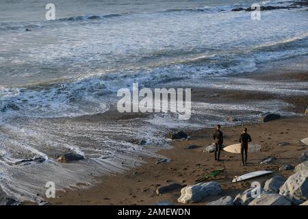 Aberystwyth Ceredigion UK 10 gennaio 2019: Due surfboards con tavole da surf sulla spiaggia che si preparano ad unirsi al loro amico già in mare Foto Stock