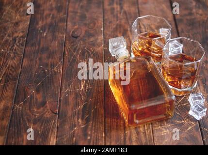 Bottiglia di whisky con due bicchieri posti su un tavolo rustico in legno Foto Stock
