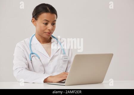 Ritratto di bella medico femminile utilizzando il computer portatile mentre seduto su sfondo bianco, copia spazio Foto Stock