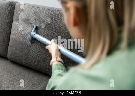 donna pulisce il divano in tessuto con un pulitore a vapore a casa Foto Stock