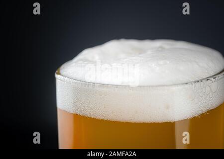 Birra artigianale in vetro fresco e freddo con schiuma bianca sulla parte superiore su sfondo nero con spazio per il testo. Birra schiumosa al grano o lager su sfondo scuro Foto Stock