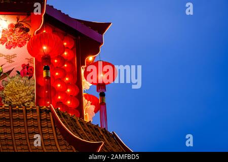 Lanterne rosse cinesi lunari nuovo anno decorazioni appese sul tetto del tempio con cielo blu scuro sullo sfondo. Foto Stock