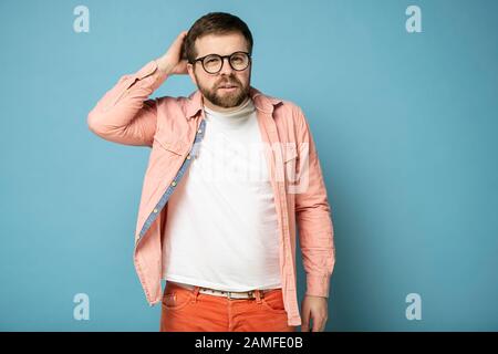 Uomo barbuto in occhiali perplesso, sta cercando di ricordare qualcosa o risolvere qualche problema. Foto Stock