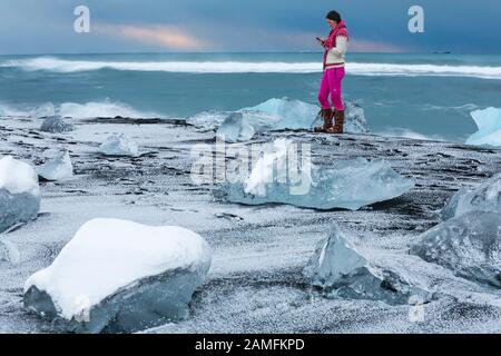 Donna turistica in spiaggia a Jokulsarlon Spiaggia Glaciale, Diamond spiaggia, Islanda nel mese di gennaio - iceberg iceberg Foto Stock