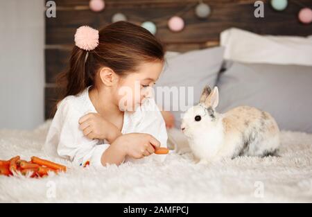 Ragazza sdraiata sul letto e alimentando il coniglio Foto Stock