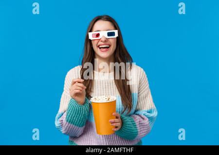 Ragazza che guarda la commedia nel cinema. Spensierata giovane bruna donna felice in maglione invernale, godendo divertente film, ridere fuori forte mangiare popcorn, indossare Foto Stock
