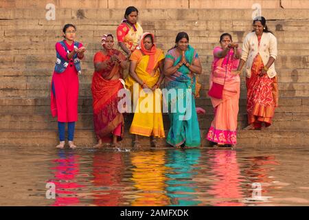 Varanasi, INDIA, 18 GENNAIO 2019 : un gruppo di donne che indossano abiti tradizionali colorati prega prima di iniziare un bagno spirituale all'alba lungo Foto Stock