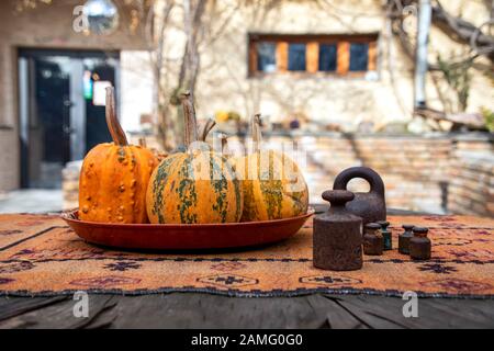 Zucche mature giacenti su un piatto e vecchi pesi metallici per scale su un tavolo di legno vicino Foto Stock