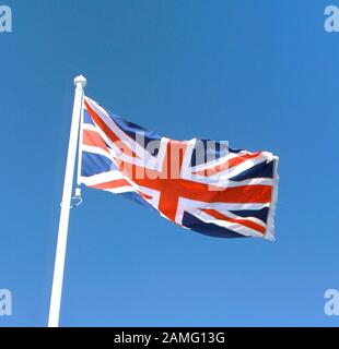 Bandiera dell'Unione Jack del Regno Unito che vola in un cielo blu brillante, Inghilterra. Foto Stock