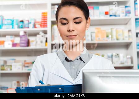 Bella farmacista scrivere negli appunti in farmacia Foto Stock