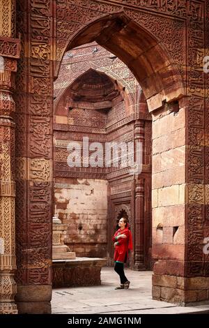 Donna in abito rosso a archi scolpiti e porta della tomba al Qutub Minar complesso a Nuova Delhi, India Foto Stock