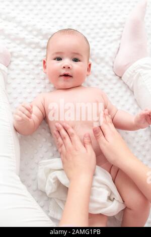 Baby massaggio. Terapista del sesso femminile massaggiando delicatamente neonato ragazzo. Madre di applicare la lozione per il corpo al suo neonato bimbo. Massaggio neonato vista superiore backgro Foto Stock