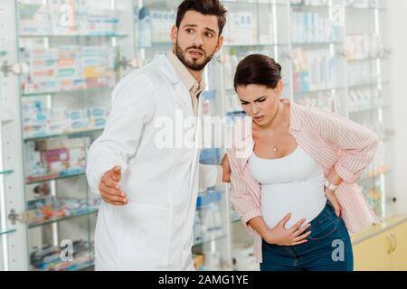 Farmacista aiutare a donna incinta con dolore in farmacia Foto Stock