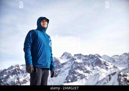 Ritratto di scalatore asiatico in giacca blu su alte montagne innevate sullo sfondo. Arrampicata all'aperto e concetto di alpinismo. Foto Stock