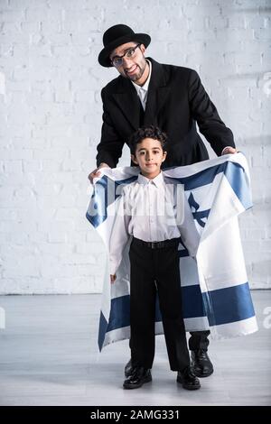 sorridente padre ebreo che tiene la bandiera di israele e figlio carino che guarda la macchina fotografica Foto Stock