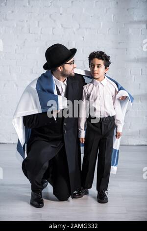 sorridendo padre ebreo e figlio carino con bandiera d'israele che si guarda l'un l'altro Foto Stock