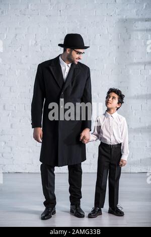 sorridendo padre ebreo e figlio carino che tiene le mani e si guarda l'un l'altro Foto Stock