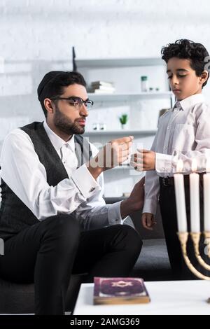 padre ebreo che dà collana a figlio carino in appartamento Foto Stock