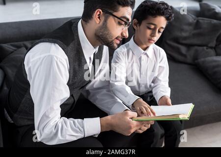 bel libro di lettura di padre ebreo e figlio in appartamento Foto Stock