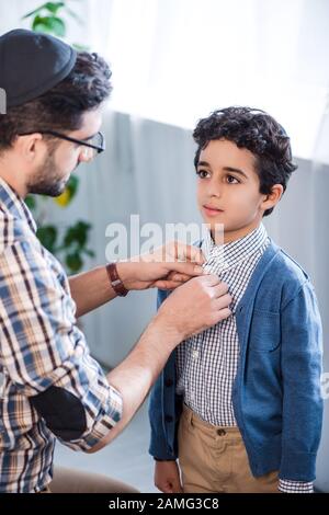 il padre ebreo buttonifica la camicia del figlio cute nell'appartamento Foto Stock