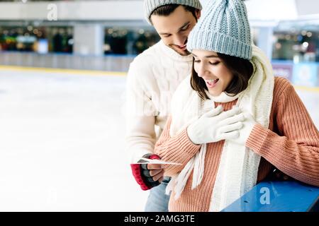 felice uomo che dà biglietto di auguri il giorno valentines a donna eccitata sulla pista di pattinaggio Foto Stock